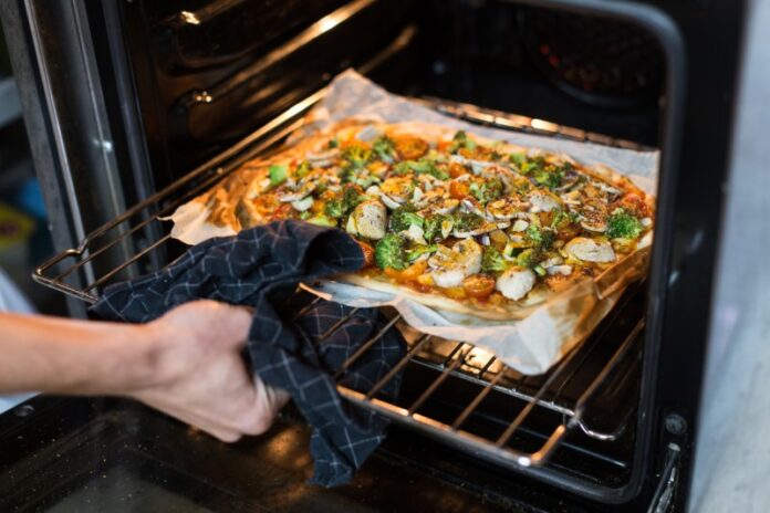 Cook holds homemade pizza on wooden board Sekrety domowego pizzaiolo – jak opanować kamień szamotowy i cyrkulację ciepła w piecu